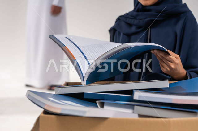 بورتريه مقرب لامرأة خليجية سعودية عربية محجبة ، اختيار كتاب من صندوق التبرعات  ، تبرعات ومبادرات انسانية ، اعمال خيرية اسلاميه في السعودية ، توفير الكتب التعليميه للمحتاجين ، خلفية بيضاء.