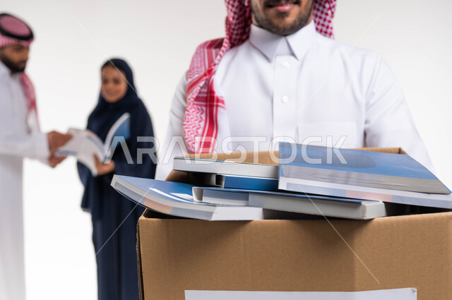 التبرع بالكتب الفائضة ، بورتريه مقرب لرجل عربي خليجي سعودي يرتدي الزي التقليدي يحمل صندوق مليء بالكتب المفيدة، توفير الكتب للمحتاجين ، وضع الكتب في حاوية الورق ، اعادة تدوير واستخدام الكتب ، اعمال خيرية اسلاميه في السعودية ، خلفية بيضاء.
