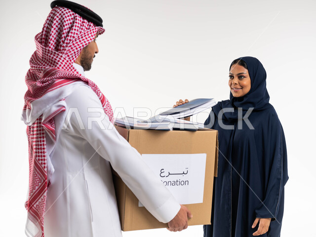 بورتريه لرجل ومرأة عربيان خليجيان سعوديان ، رجل يحمل صندوق مليء بالكتب المفيدة ، وضع الكتب في حاوية الورق ، اعادة التدوير، توفير الكتب التعليميه للمحتاجين، تبرعات  ومبادرات انسانية  ، اعمال خيرية اسلاميه  في السعودية ، خلفية بيضاء.