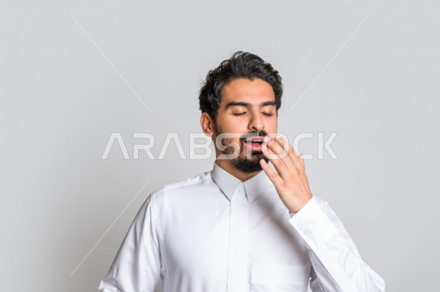 بورتريه لرجل عربي سعودي خليجي باللباس التقليدي السعودي , إيماءات وجه ويدين تدل على النعاس , الإحساس بالتعب والتثاؤب , الحاجة للنوم والراحة , الكسل والخمول ,خلفية بيضاء .