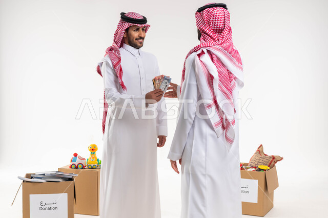 بورتريه لرجل سعودي خليجي عربي يرتدي الزري السعودي التقليدي يقوم بتقديم مجموعة من النقود الورقية ، العبادة والتقرب الى الله ، العطاء والصدقة في شهر رمضان ، جمعيات خيرية في السعودية ، خلفية بيضاء.