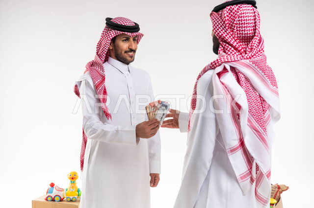 المساعدات والتبرعات في شهر رمضان  ، بورتريه لرجل عربي سعودي خليجي يرتدي الزي التقليدي يقوم بتقديم مجموعة من النقود الورقية ، العبادة والتقرب الى الله ، جمعيات خيرية اسلامية في السعودية ، خلفية بيضاء.