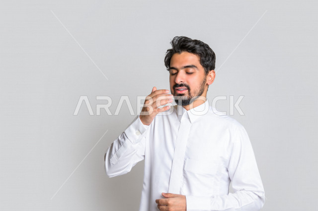 بورتريه لرجل عربي سعودي خليجي باللباس التقليدي السعودي , إيماءات وجه ويدين تدل على النعاس , الإحساس بالتعب والتثاؤب , الحاجة للنوم والراحة , الكسل والخمول ,خلفية بيضاء .