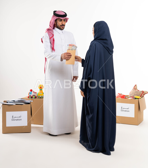 الجمعيات الخيرية في السعودية ، بورتريه لرجل عربي سعودي خليجي يرتدي الزي التقليدي يقدم المساعدة لامرأة متعففة ، اخراج زكاة المال للمحتاجين ، العطاء و الصدقة في شهر رمضان ، صورة الجسم بالطول الكامل  ، خلفية بيضاء.