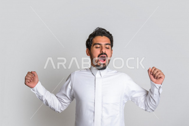 بورتريه لرجل عربي سعودي خليجي باللباس التقليدي السعودي , إيماءات وجه ويدين تدل على النعاس , الإحساس بالتعب والتثاؤب , الحاجة للنوم والراحة , الكسل والخمول ,خلفية بيضاء .