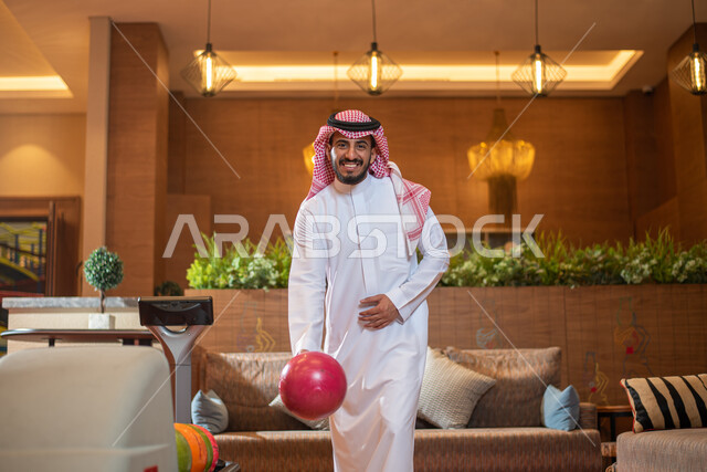 قضاء أوقات ممتعة في ممارسة لعبة البولينج ، أنشطة رياضية ترفيهية ، رجل عربي خليجي سعودي يرتدي الزي السعودي التقليدي يمارس لعبة البولينج ( الكردحه ) ،في أماكن ترفيهية ، مضمار البولينج ، ملعب البولينج