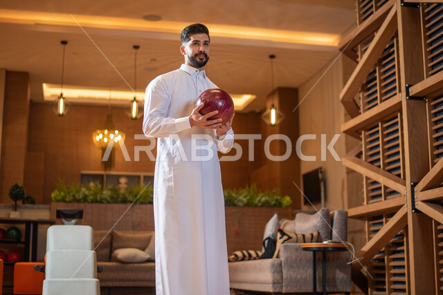 أنشطة رياضية ترفيهية ، رجل عربي خليجي سعودي يرتدي الزي السعودي التقليدي يمارس لعبة البولينج ( الكردحه ) ،في أماكن ترفيهية ، مضمار البولينج ، ملعب البولينج ، قضاء أوقات ممتعة في ممارسة لعبة البولينج