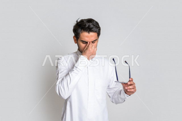 بورتريه لرجل عربي سعودي خليجي يرتدي الثوب السعودي, ايماءات وجه ويدين تدل على الشعور بالحزن والإحباط, الرغبه بالبكاء, الندم على شيء ما, الخساره والفشل , خلفية بيضاء .