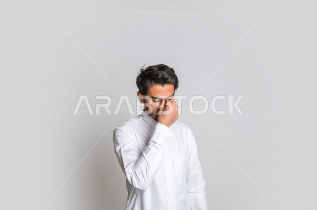 Portrait of a Saudi Arabian Gulf man wearing the Saudi dress, facial and hands gestures indicating feelings of sadness and frustration, the desire to cry, regret for something, loss and failure, white background.