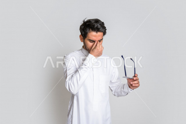 Portrait of a Saudi Arabian Gulf man wearing the Saudi dress, facial and hands gestures indicating feelings of sadness and frustration, the desire to cry, regret for something, loss and failure, white background.