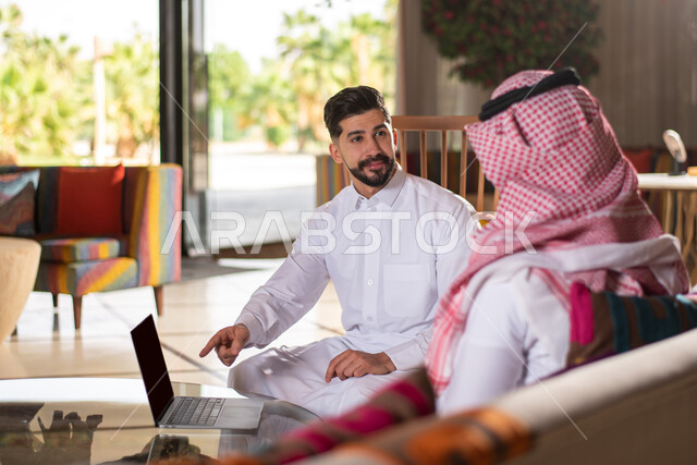 استخدام تقنيات حديثة ،  استخدام الهاتف المحمول ،ايماءات وجه تدل على السعادة والسرور ، رجلان عربيان خليجيان سعوديان يرتديان الزي السعودي التقليدي يستخدمان جهاز الجوال ، اجتماع عمل ، نقاشات وحوارات ، جلسة شبابية