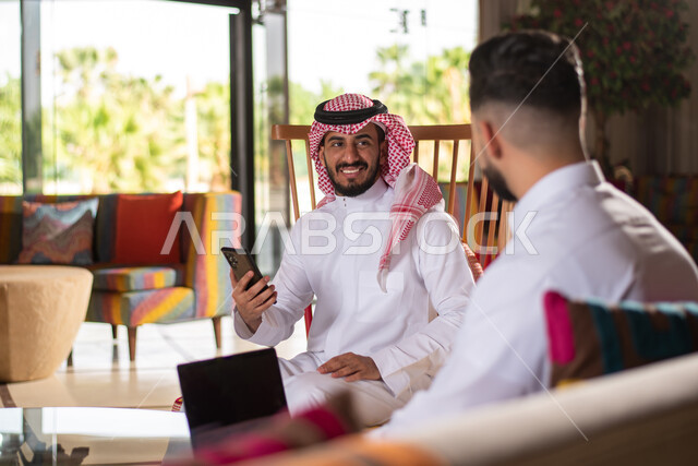 استخدام الهاتف المحمول ،ايماءات وجه تدل على السعادة والسرور ، رجلان عربيان خليجيان سعوديان يرتديان الزي السعودي التقليدي يستخدمان جهاز الجوال ، استخدام تقنيات حديثة ،  اجتماع عمل ، نقاشات وحوارات ، جلسة شبابية