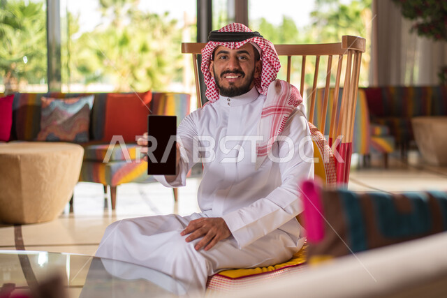 Displaying a blank black screen, a Saudi Arabian Gulf man in traditional Saudi dress using a mobile phone, working remotely, completing work tasks, surfing the Internet, using modern technologies.
