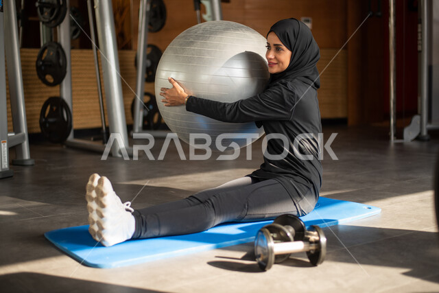 نشاط وحركة ، لياقة ورشاقة ، صالة الألعاب الرياضية ، شابة عربية خليجية سعودية في النادي الرياضي  ترتدي الملابس الرياضية السوداء وتقوم بتمارين رفع الاوزان