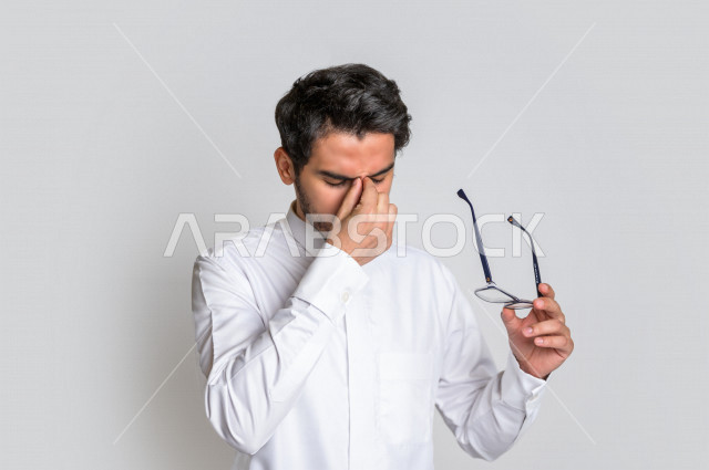بورتريه لرجل عربي سعودي خليجي يرتدي الثوب السعودي, ايماءات وجه ويدين تدل على الشعور بالحزن والإحباط, الرغبه بالبكاء, الندم على شيء ما, الخساره والفشل , خلفية بيضاء .