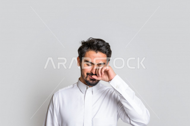 بورتريه لرجل عربي سعودي خليجي يرتدي الثوب السعودي, ايماءات وجه ويدين تدل على الشعور بالحزن والإحباط, الرغبه بالبكاء, الندم على شيء ما, الخساره والفشل , خلفية بيضاء .