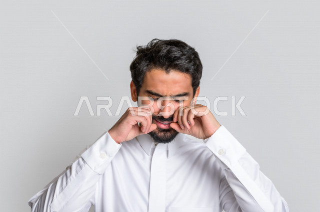 بورتريه لرجل عربي سعودي خليجي يرتدي الثوب السعودي, ايماءات وجه ويدين تدل على الشعور بالحزن والإحباط, الرغبه بالبكاء, الندم على شيء ما, الخساره والفشل , خلفية بيضاء .