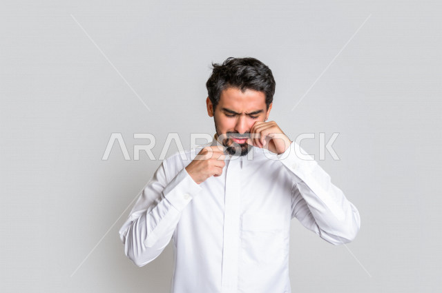 بورتريه لرجل عربي سعودي خليجي يرتدي الثوب السعودي, ايماءات وجه ويدين تدل على الشعور بالحزن والإحباط, الرغبه بالبكاء, الندم على شيء ما, الخساره والفشل , خلفية بيضاء .