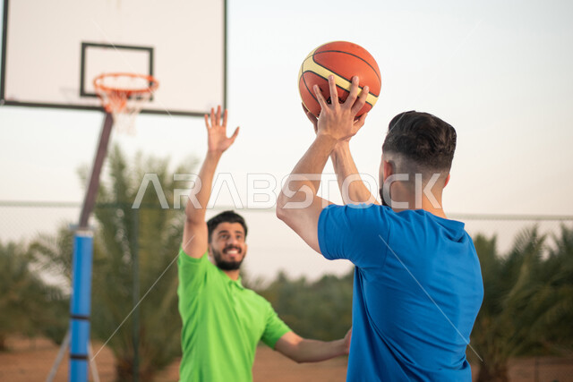 منافسات وتحديات والقيام بنشاط بدني في الهواء الطلق ، الاستعداد لتسجيل الأهداف ، انشطة ورياضات شبابية، صديقان عربيان خليجيان سعوديان يلعبان كرة السلة في الملاعب العامة ، أندية و تشجيع