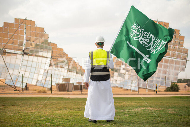 يوم العلم ,صورة من الخلف لمهندس عربي خليجي سعودي يحمل علم المملكة العربية السعودية ، محطات توليد الكهرباء عبر الطاقة الشمسية، الاحتفال باليوم الوطني السعودي 92، ستلايت والواح الطاقة الطبيعية المتجددة ,صورة الجسم بالطول الكامل , رؤية ومشاريع مستقبلية جديدة