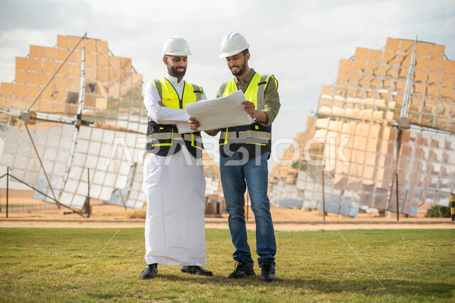 مهندسان عربيان خليجيان سعوديان يشرفان على محطات الطاقة الشمسية في السعودية، إرتداء خوذة وسترة الحماية الخاصة بالعمل، مخططات وتصاميم هندسية، حوارات ونقاشات عمل ،محطات الطاقة الشمسية المتجددة، الواح وستلايت انتاج الطاقة الكهربائية , صورة الجسم بالطول الكامل