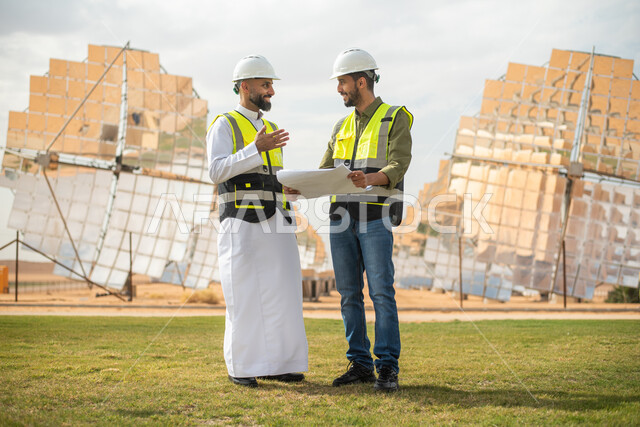 A back image of two Saudi Arab Gulf engineers supervising solar power plants in Saudi Arabia, wearing a helmet and work protection jacket, engineering plans and designs, business dialogues and discussions, renewable solar energy stations, panels and satel
