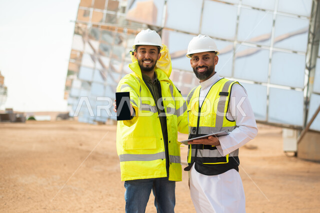استخدام الهاتف المحمول , مهندسان عربيان خليجيان سعوديان يشرفان على محطات الطاقة الشمسية في السعودية، إرتداء خوذة وسترة الحماية الخاصة بالعمل، مخططات وتصاميم هندسية، حوارات ونقاشات عمل ،  محطات الطاقة الشمسية المتجددة، الواح وستلايت انتاج الطاقة الكهربائية