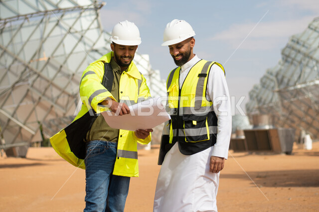 مهندسان عربيان خليجيان سعوديان يشرفان على محطات الطاقة الشمسية في السعودية، إرتداء خوذة وسترة الحماية الخاصة بالعمل، مخططات وتصاميم هندسية، حوارات ونقاشات عمل ،  محطات الطاقة الشمسية المتجددة، الواح وستلايت انتاج الطاقة الكهربائية , تطور التقنية والتكنولو