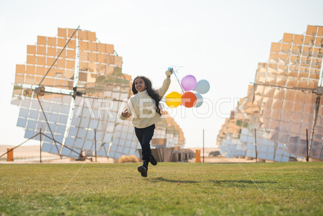 ستلايت وألواح الطاقة الطبيعية المتجددة ، فتاة عربية خليجية سعودية تحمل في يدها بالونات ملونة ، محطات توليد الكهرباء عبر الطاقة الشمسية  ، رؤية ومشاريع مستقبلية جديدة ، نزهة في الهواء الطلق , أنشطة ترفيهية للاطفال .