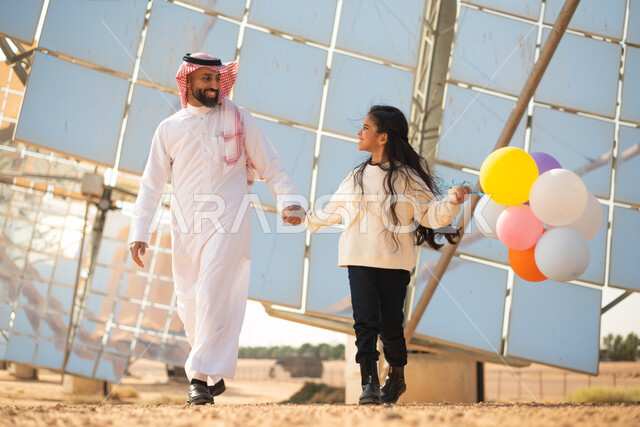 رجل عربي خليجي سعودي يقضي وقته مع وابنته ، توليد الطاقة الكهربائية عبر الواح الطاقة الشمسية , ستلايات وألواح طاقة طبيعية متجددة , صورة الجسم بالطول الكامل , رؤية ومشاريع مستقبلية جديدة .