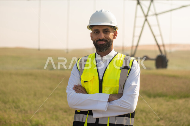 صورة مقربة لمهندس زراعي عربي خليجي سعودي يشرف على حقل زراعي، الاشجار والنباتات الخضراء، زراعة المستقبل، محاصيل زراعية، إرتداء خوذة وسترة الحماية، البيئة والتنمية، القطاع الزراعي، مستقبل تكنولوجيا الزراعة.
