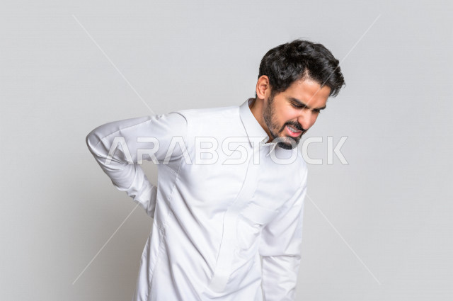 Portrait of a Saudi Arabian Gulf man wearing the Saudi dress, facial and hands gestures indicating pain, back and spine pain, feeling sick, fatigue and exhaustion, needing treatment, asking for help, white background.