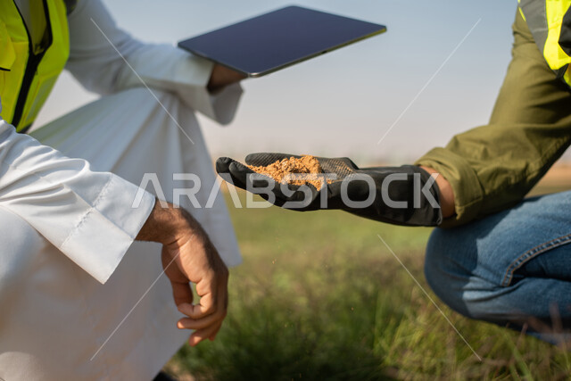 A close-up of two Saudi Arabian Gulf agricultural engineers examining the soil, using technology and technology to develop the future of the agricultural sector, improving the production of agricultural crops in Saudi Arabia, and developing farms and gree