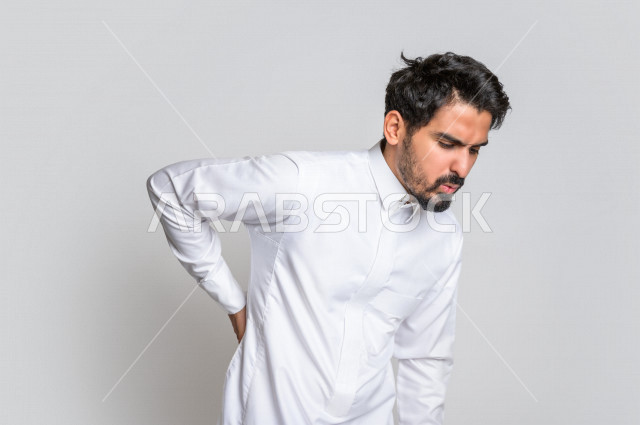 بورتريه لرجل عربي سعودي خليجي يرتدي الثوب السعودي, إيماءات وجه ويدين تدل على الشعور بالألم , آلآم الظهر والعمود الفقري , الإحساس بالمرض , التعب والإرهاق , الحاجه للعلاج , طلب المساعده , خلفية بيضاء .