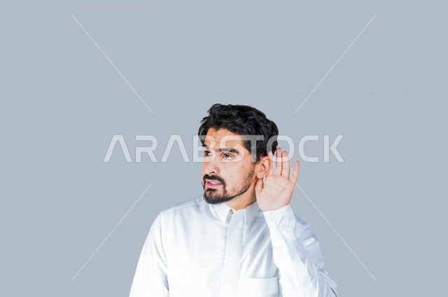 بورتريه لرجل عربي سعودي خليجي يرتدي الثوب السعودي, إيماءات يد تدل على الإنصات, حسن الإستماع, التركيز على الكلام, محاولة التجسس والتنصت, سماع الأسرار , خلفية بيضاء .
