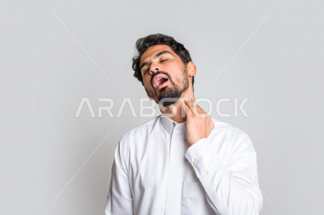 بورتريه لرجل عربي سعودي خليجي يرتدي الثوب السعودي, إيماءات وجه ويدين تدل على الإحساس بالوجع , ألم بالرقبة , الإحساس بالمرض , التعب والإرهاق , الحاجه للعلاج , طلب المساعده , خلفية بيضاء .