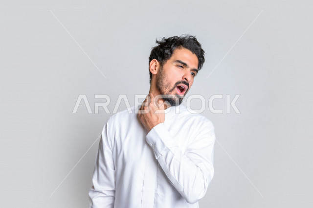 بورتريه لرجل عربي سعودي خليجي يرتدي الثوب السعودي, إيماءات وجه ويدين تدل على الإحساس بالوجع , ألم بالرقبة , الإحساس بالمرض , التعب والإرهاق , الحاجه للعلاج , طلب المساعده , خلفية بيضاء .