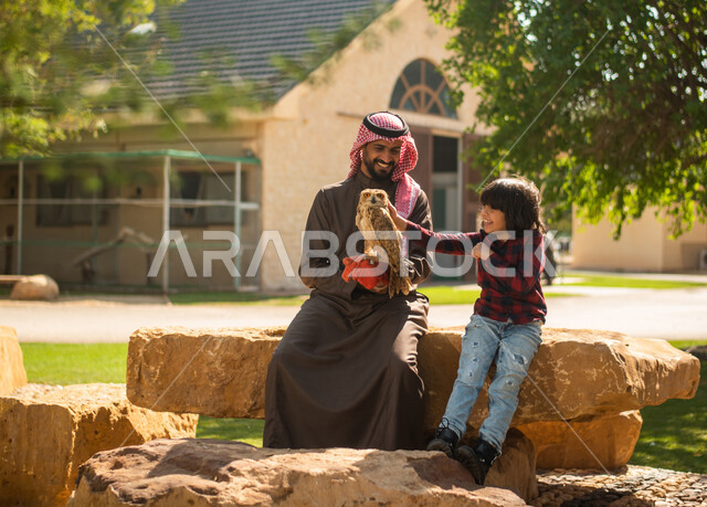 ايماءات تدل على السعادة, رجل عربي سعودي خليجي مع إبنه، قضاء أوقات ممتعة في حديقة الحيوانات في المملكة العربية السعودية، أماكن سياحية ترفيهية، أنشطة ترفيهية مع الطيور، تربية وتدريب الطيور الجارحة في المحمية الطبيعية، طائر البومة