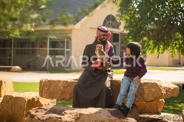 ايماءات تدل على السعادة, رجل عربي سعودي خليجي مع إبنه، قضاء أوقات ممتعة في حديقة الحيوانات في المملكة العربية السعودية، أماكن سياحية ترفيهية، أنشطة ترفيهية مع الطيور، تربية وتدريب الطيور الجارحة في المحمية الطبيعية، طائر البومة