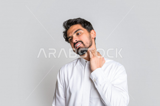 بورتريه لرجل عربي سعودي خليجي يرتدي الثوب السعودي, إيماءات وجه ويدين تدل على الإحساس بالوجع , ألم بالرقبة , الإحساس بالمرض , التعب والإرهاق , الحاجه للعلاج , طلب المساعده , خلفية بيضاء .
