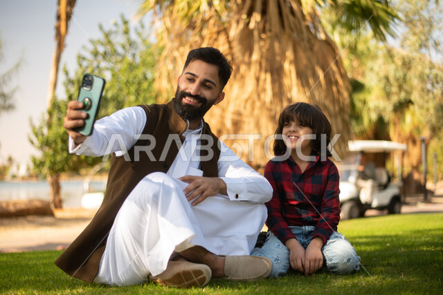 طفل ووالده عربيان سعوديان خليجيان , التقاط صور سيلفي عبر الهاتف المحمول, الاستمتاع باللعب , قضاء أوقات ممتعة في احد الحدائق العامة في المملكة العربية السعودية، أماكن سياحية ترفيهية بالسعودية، فعاليات ترفيهية عائلية