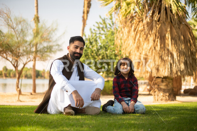 طفل ووالده عربيان خليجيان سعوديان , النظر الى الكاميرا,  الاستمتاع باللعب , قضاء أوقات ممتعة في احد الحدائق العامة في المملكة العربية السعودية، أماكن سياحية ترفيهية بالسعودية، فعاليات ترفيهية عائلية