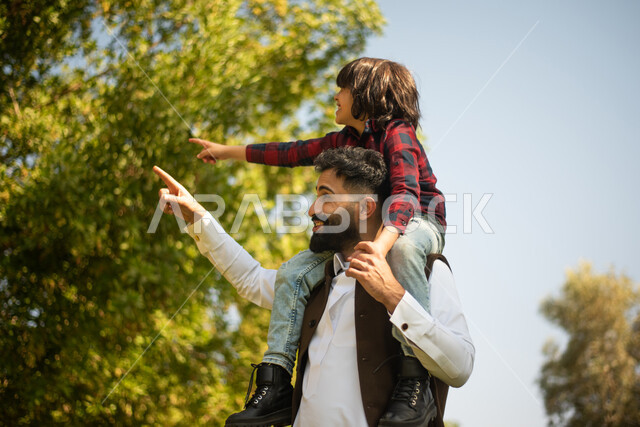 اب يحمل ابنه على ظهره ، قضاء وقت ممتع مع الابناء في احدى الحدائق, الاشارة الى شيء ما, عطلة صيفية، نزهه في الحدائق العامة، الاستمتاع في الهواء الطلق، جولة في الطبيعة الخضراء، مزرعة واستراحات، أنشطة ترفيهية عائلية
