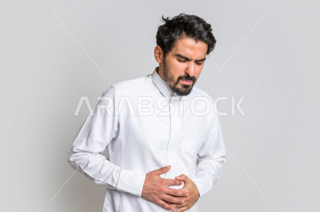 Portrait of a Saudi Arabian Gulf man wearing the Saudi dress, facial and hands gestures indicating fatigue, abdominal pain, feeling sick and poisoning, fatigue and exhaustion, colon aches, need for treatment, asking for help, white background.