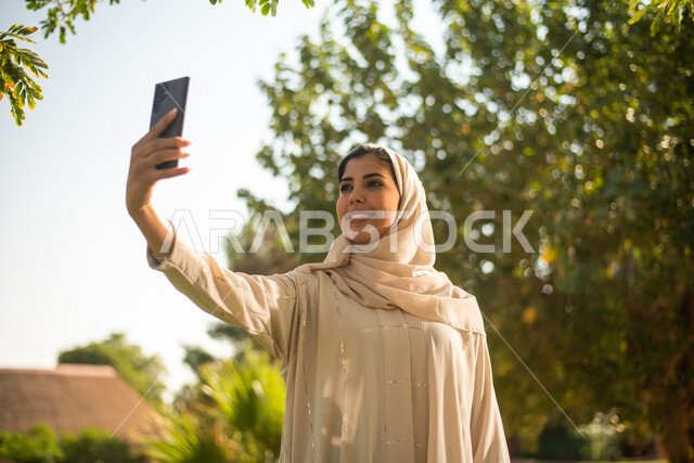 امرأة  عربية سعودية خليجية التقاط صور تذكارية باستخدام الهاتف المحمول ،  نزهه في الهواء الطلق ، جولة في الطبيعة الخضراء ، قضاء اوقات ممتعة في إحدى الحدائق العامة بالسعودية.