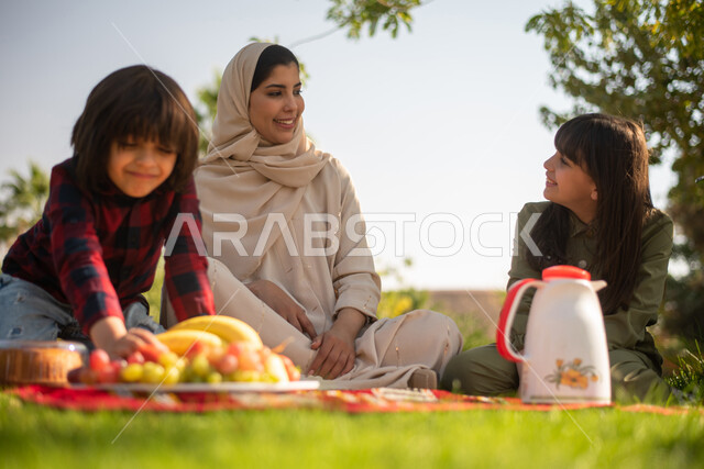 تصوير مقربة لمرأة عربية خليجية سعودية برفقة أبناءها ، قضاء اوقات ممتعة في إحدى الحدائق العامة بالسعودية ، نزهة في في الهواء الطلق ، الجلوس في الطبيعة الخضراء ، عطلة صيفية.