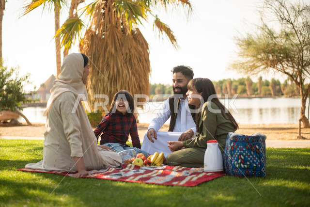 عائلة سعودية عربية خليجية الاستمتاع بقضاء اوقات ممتعة في إحدى الحدائق العامة بالسعودية ، اجواء عائلية سعيدة، نزهة في في الهواء الطلق،  الجلوس في الطبيعة الخضراء، عطلة صيفية.