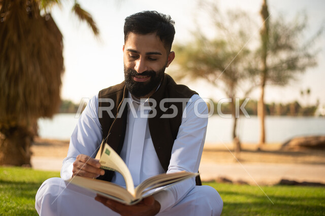 صورة مقربة لرجل  خليجي عربي سعودي يستمتع بقرأة القصص والروايات في إحدى الحدائق العامة بالسعودية ، نزهة في الهواء الطلق ، عطلة صيفية ، الجلوس في الطبيعة الخضراء.