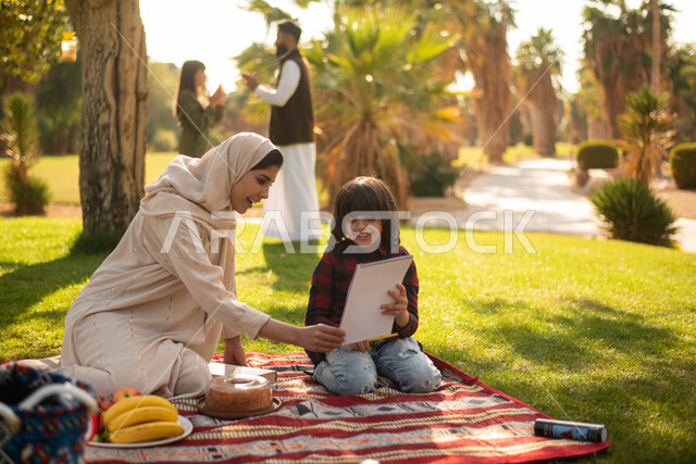 قضاء اوقات ممتعة في الهواء الطلق ، مرأة سعودية عربية خليجية برفقة ولدها  في إحدى الحدائق العامة بالسعودية ، ممارسة هواية الرسم والكتابة ،  عطلة صيفية ، الجلوس في الطبيعة الخضراء.