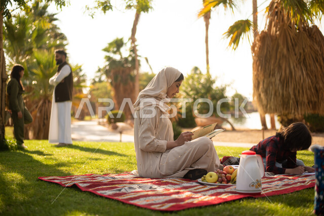 امرأة سعودية  عربية خليجية برفقة ولدها  في إحدى الحدائق العامة بالسعودية ، ممارسة هواية الرسم والكتابة ، نزهه في الهواء الطلق ، عطلة صيفية، الجلوس في الطبيعة الخضراء.